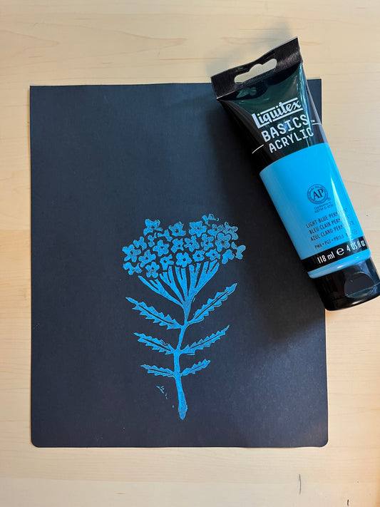A tube of blue acrylic paint resting on the top right corner of black sketch paper, featuring a blue floral design.