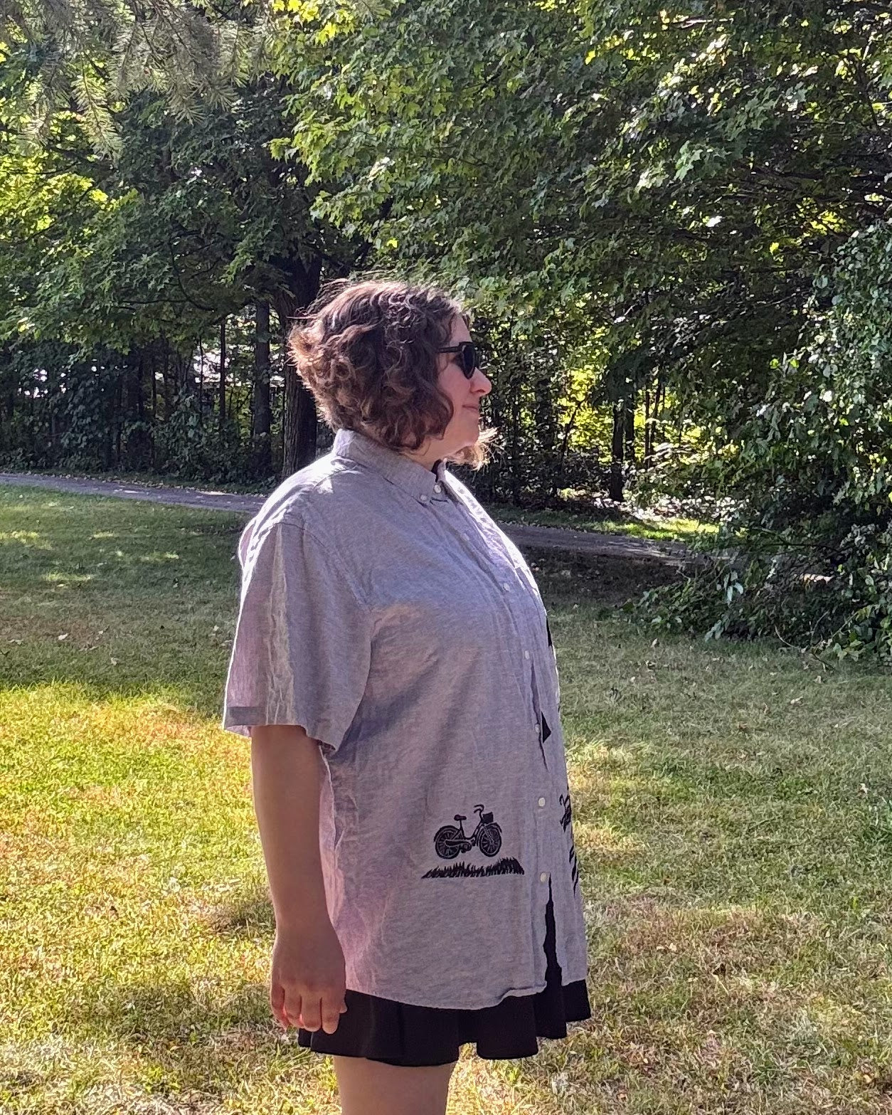 Over the Bridge; grey short sleeve top featuring a bicycle, bridge, and fairy cottage