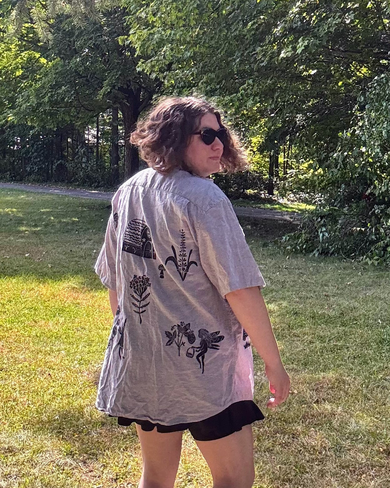 Over the Bridge; grey short sleeve top featuring a bicycle, bridge, and fairy cottage