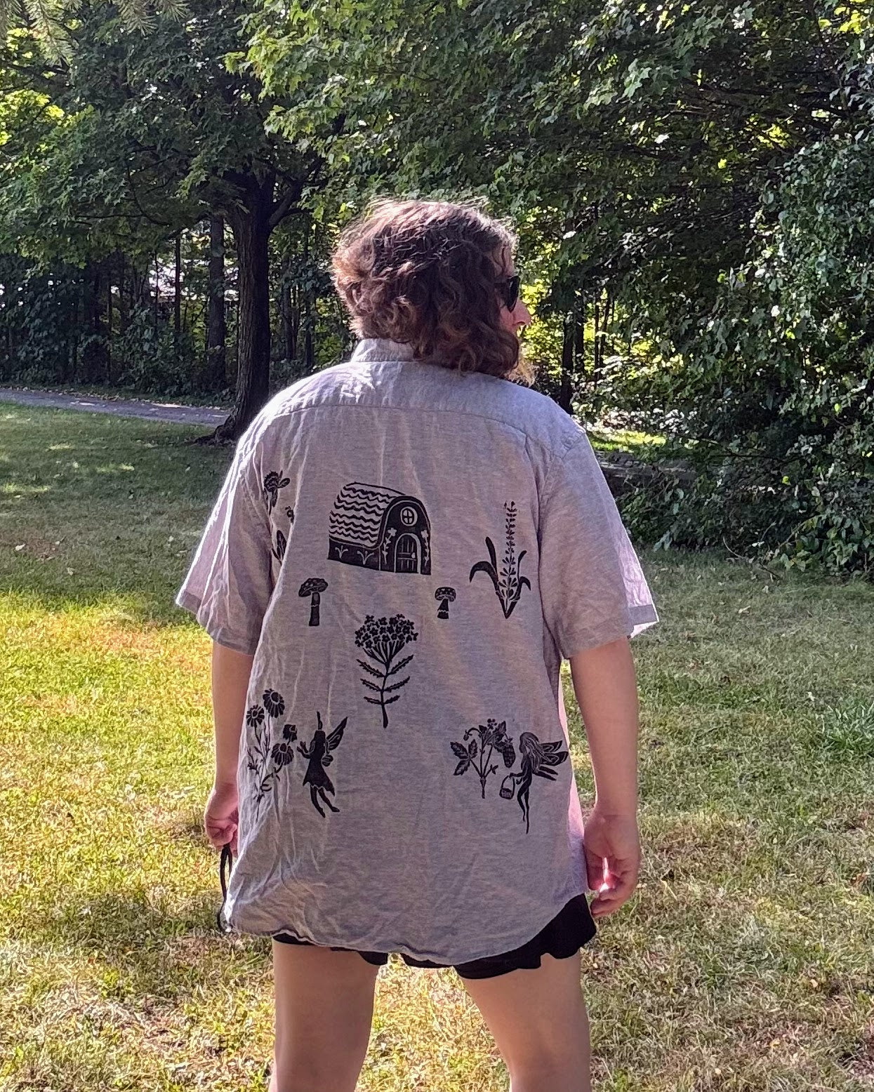 Over the Bridge; grey short sleeve top featuring a bicycle, bridge, and fairy cottage