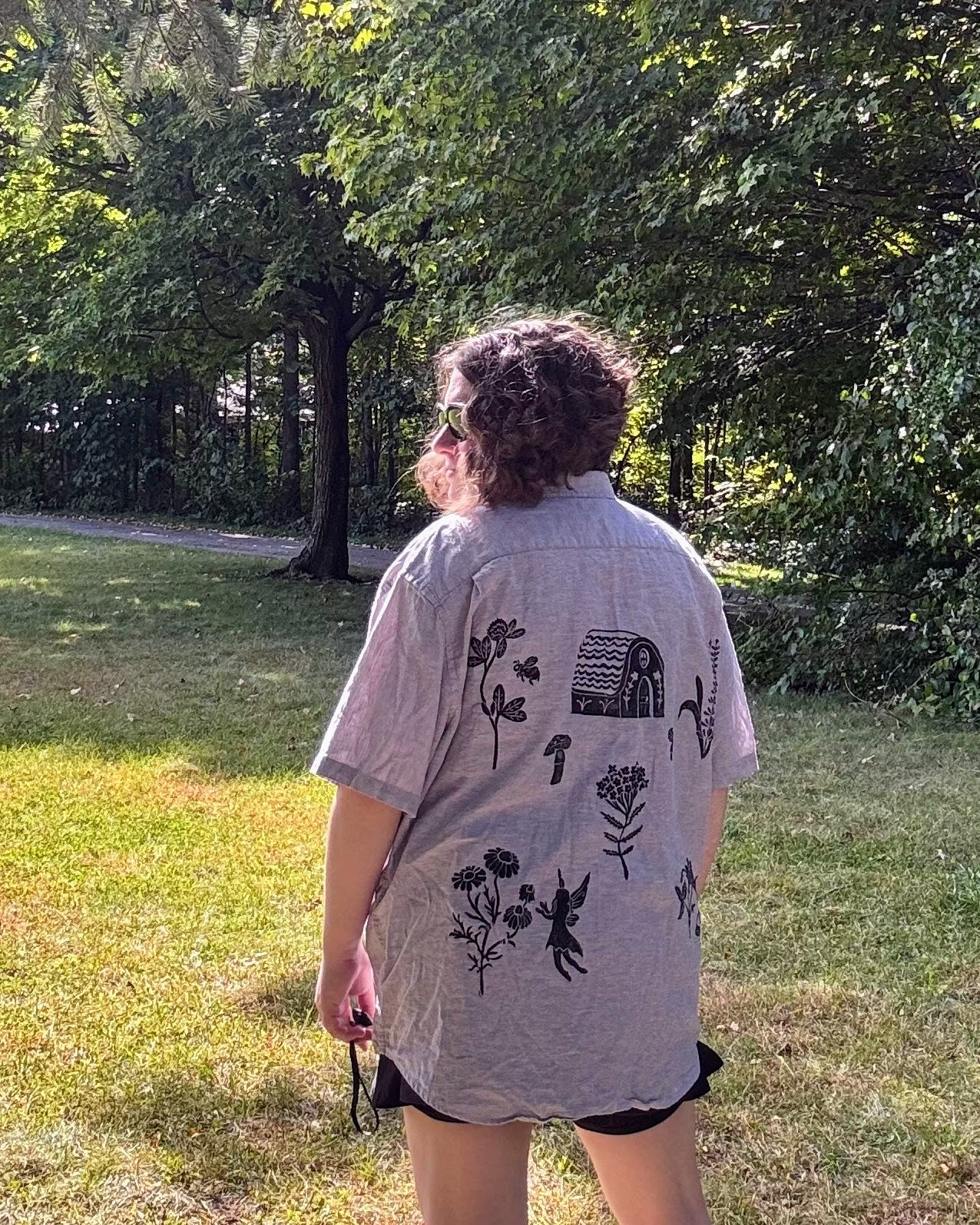 Over the Bridge; grey short sleeve top featuring a bicycle, bridge, and fairy cottage