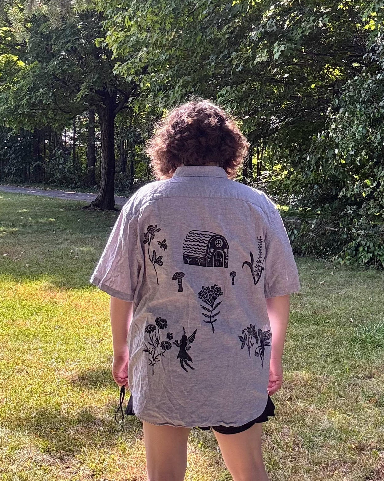 Over the Bridge; grey short sleeve top featuring a bicycle, bridge, and fairy cottage