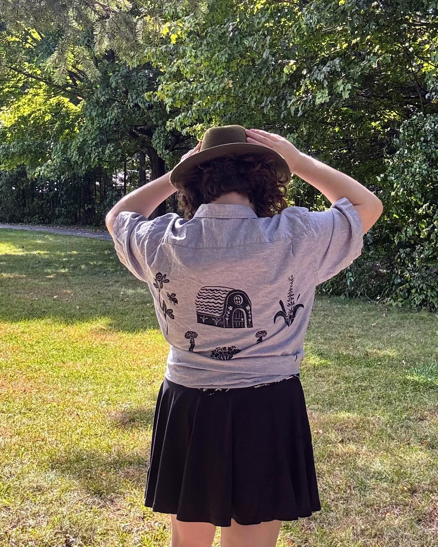 Over the Bridge; grey short sleeve top featuring a bicycle, bridge, and fairy cottage