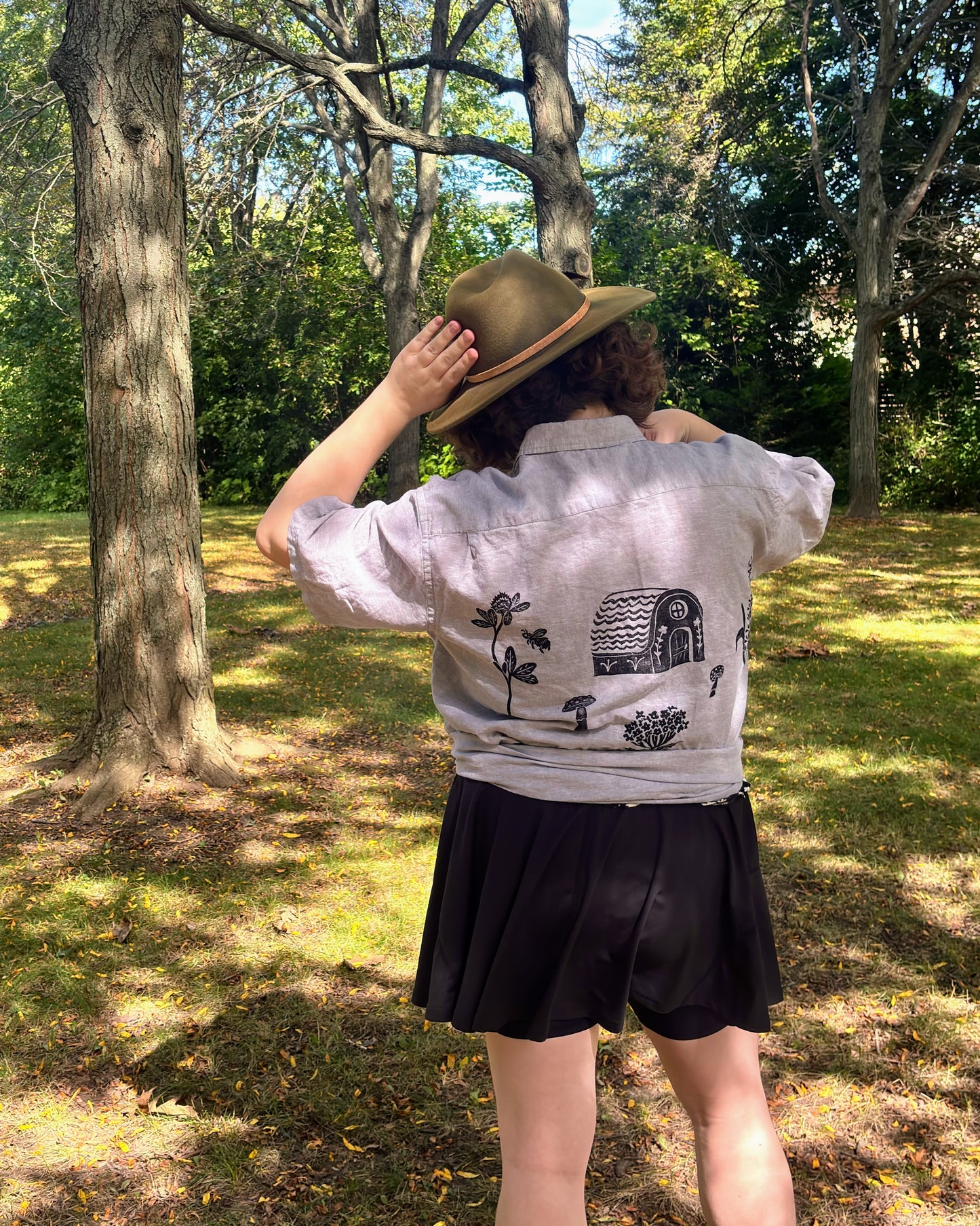 Over the Bridge; grey short sleeve top featuring a bicycle, bridge, and fairy cottage