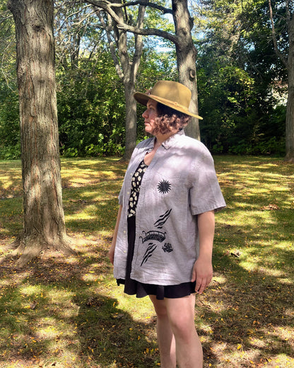 Over the Bridge; grey short sleeve top featuring a bicycle, bridge, and fairy cottage